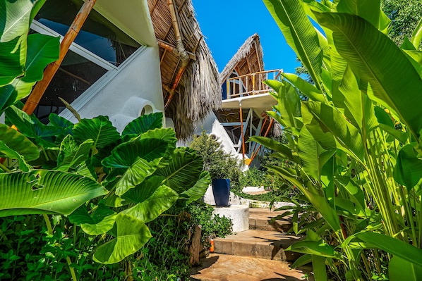 A tropical resort with a thatched-roof structure, a stone pathway, and lush greenery.