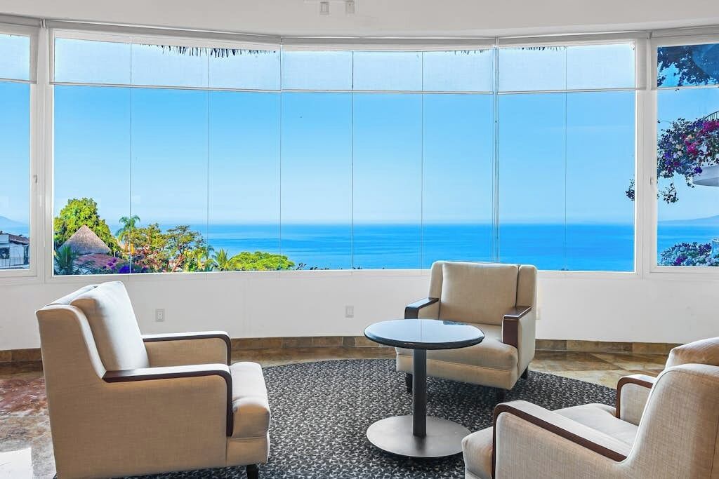 A room with a large window, two chairs, a small round table, and a patterned carpet.