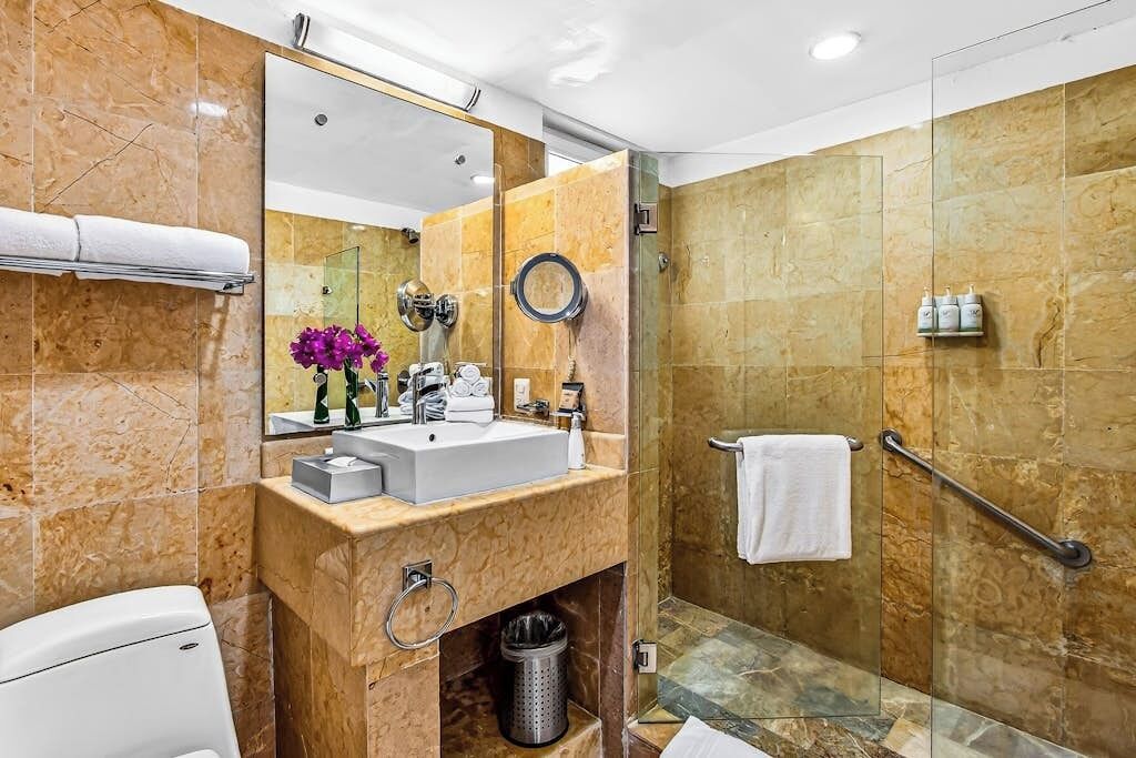 Een moderne badkamer met een grote spiegel, een wastafel, toilet, douchegedeelte en een handgreep.