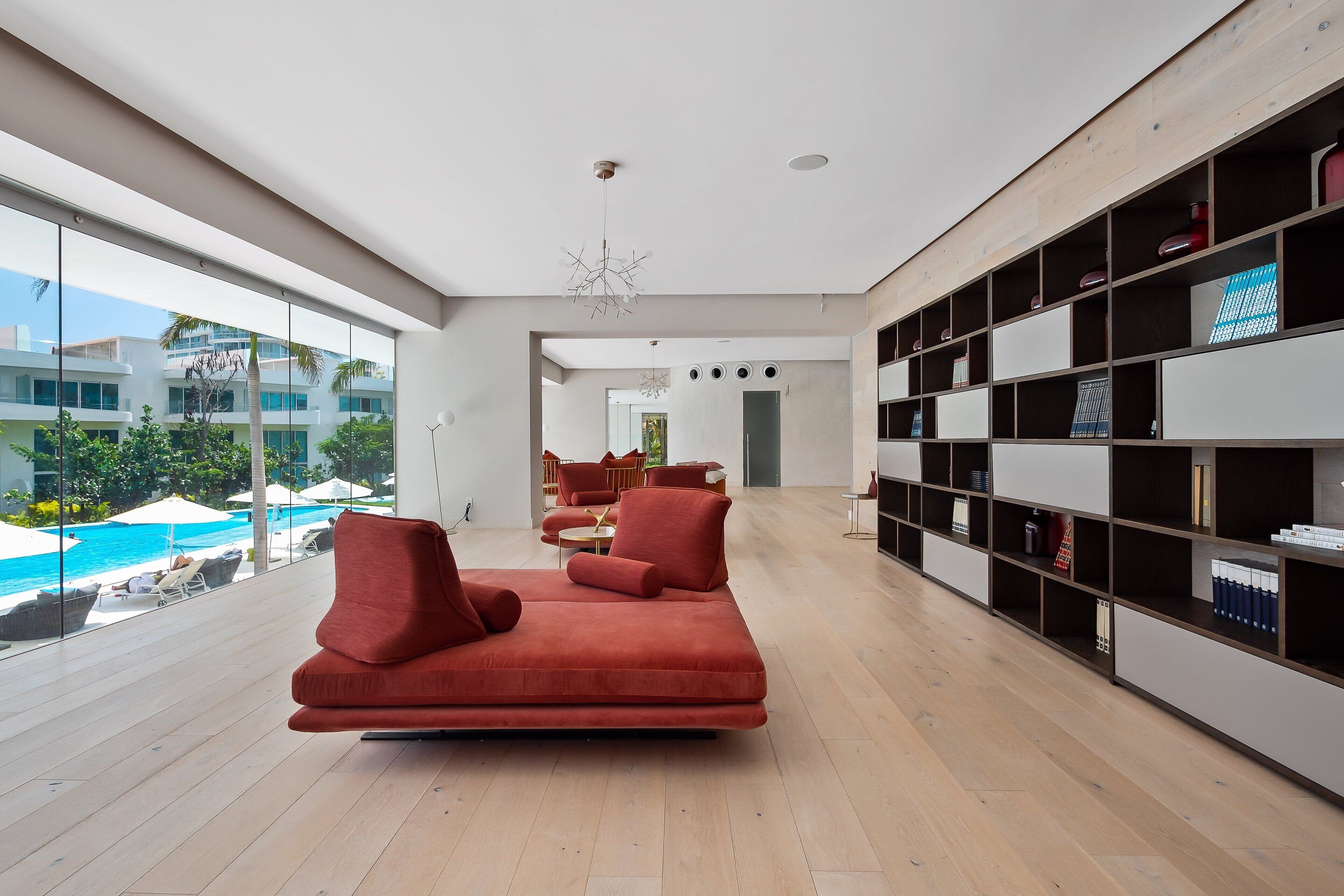 Una sala de estar moderna con un sofá rojo, una estantería y vista a una piscina.