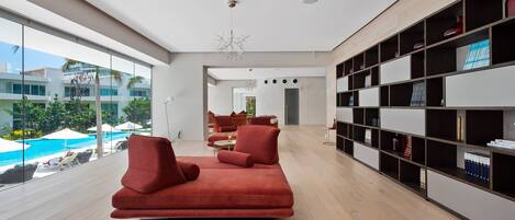 Una sala de estar moderna con un sofá rojo, una estantería y vista a una piscina.
