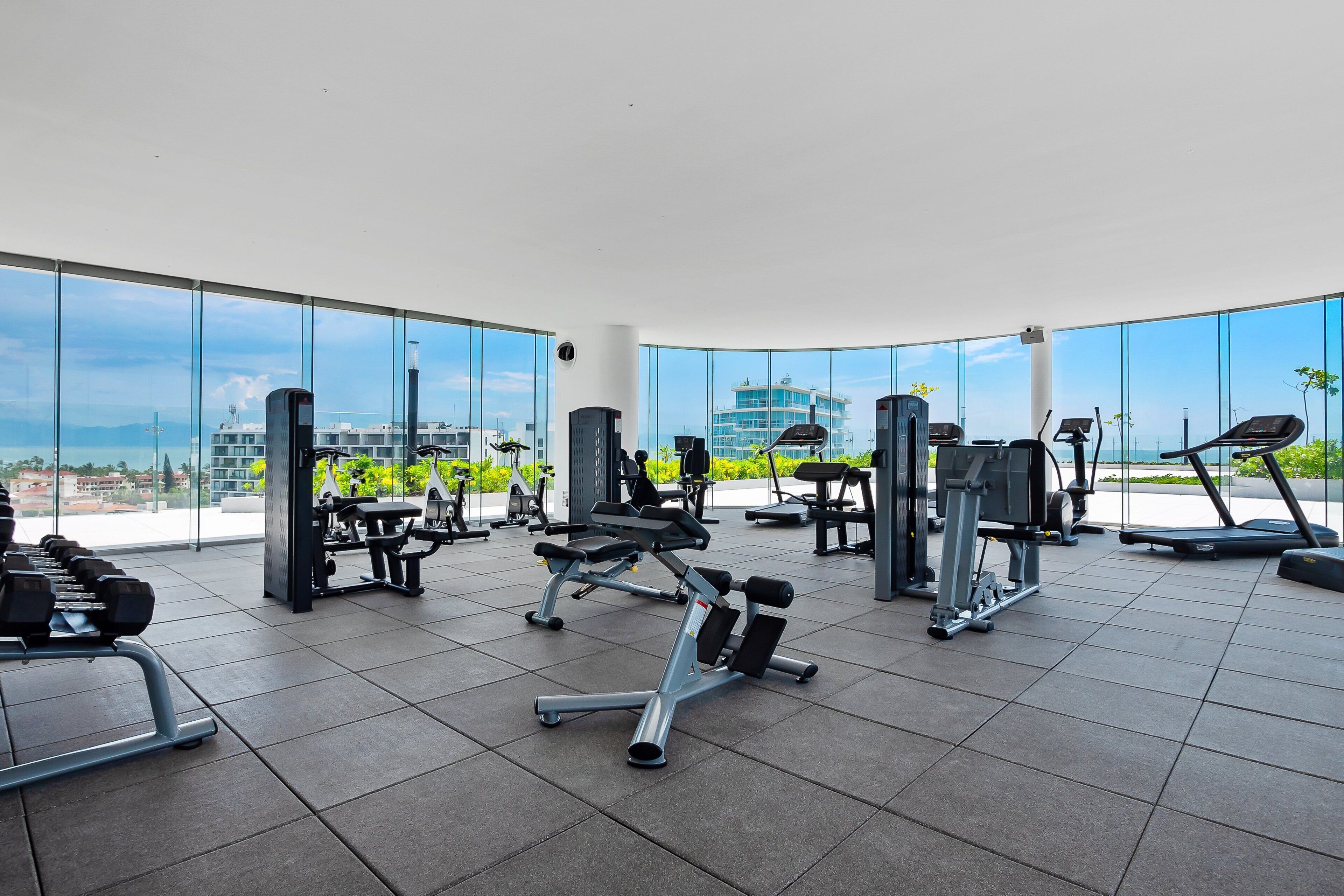 A gym with various exercise equipment, large windows, and a view of buildings.