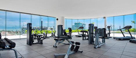 A gym with various exercise equipment, large windows, and a view of buildings.