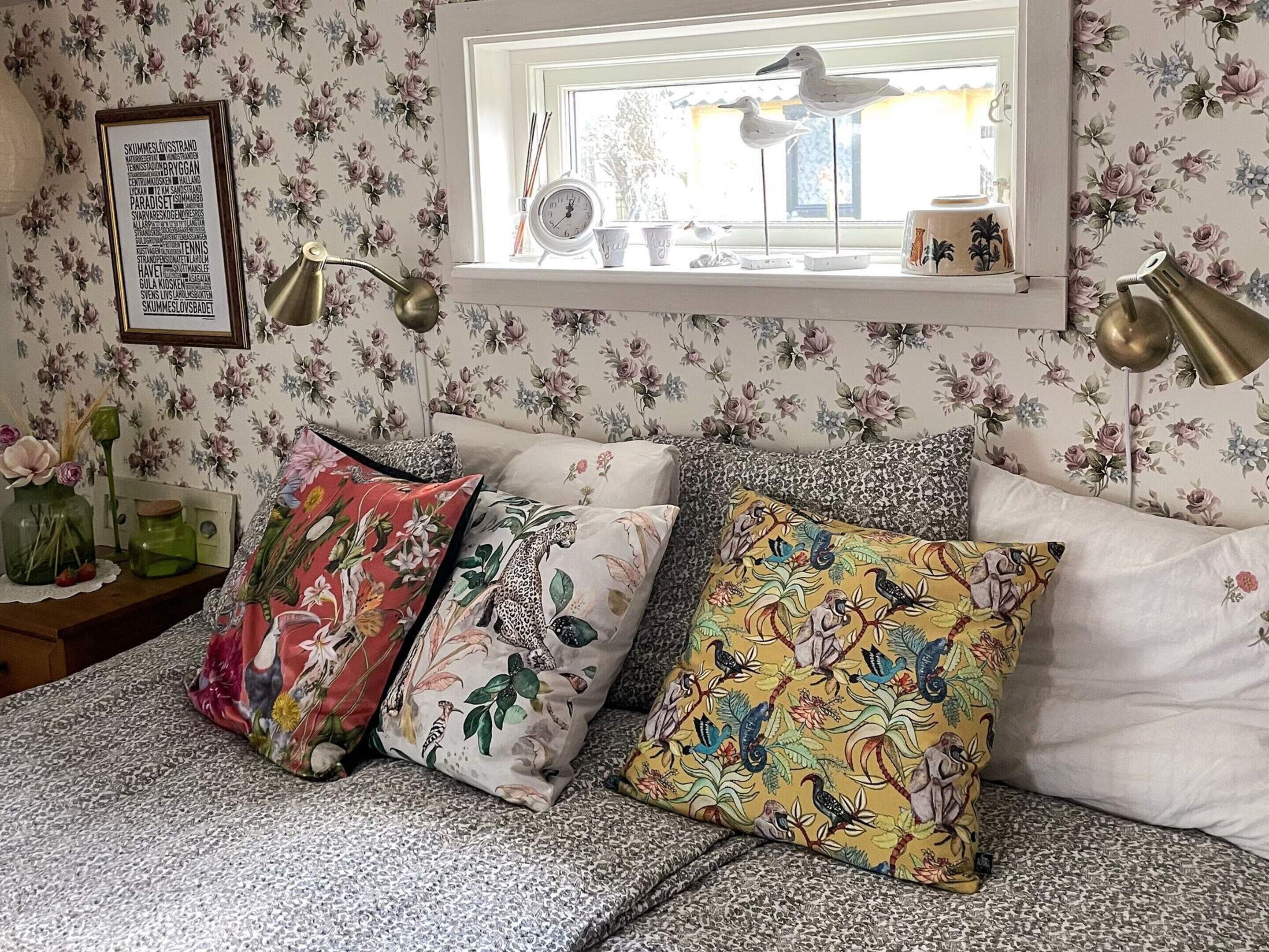 A bedroom with floral wallpaper, a framed word cloud on the wall, and a window with a view.