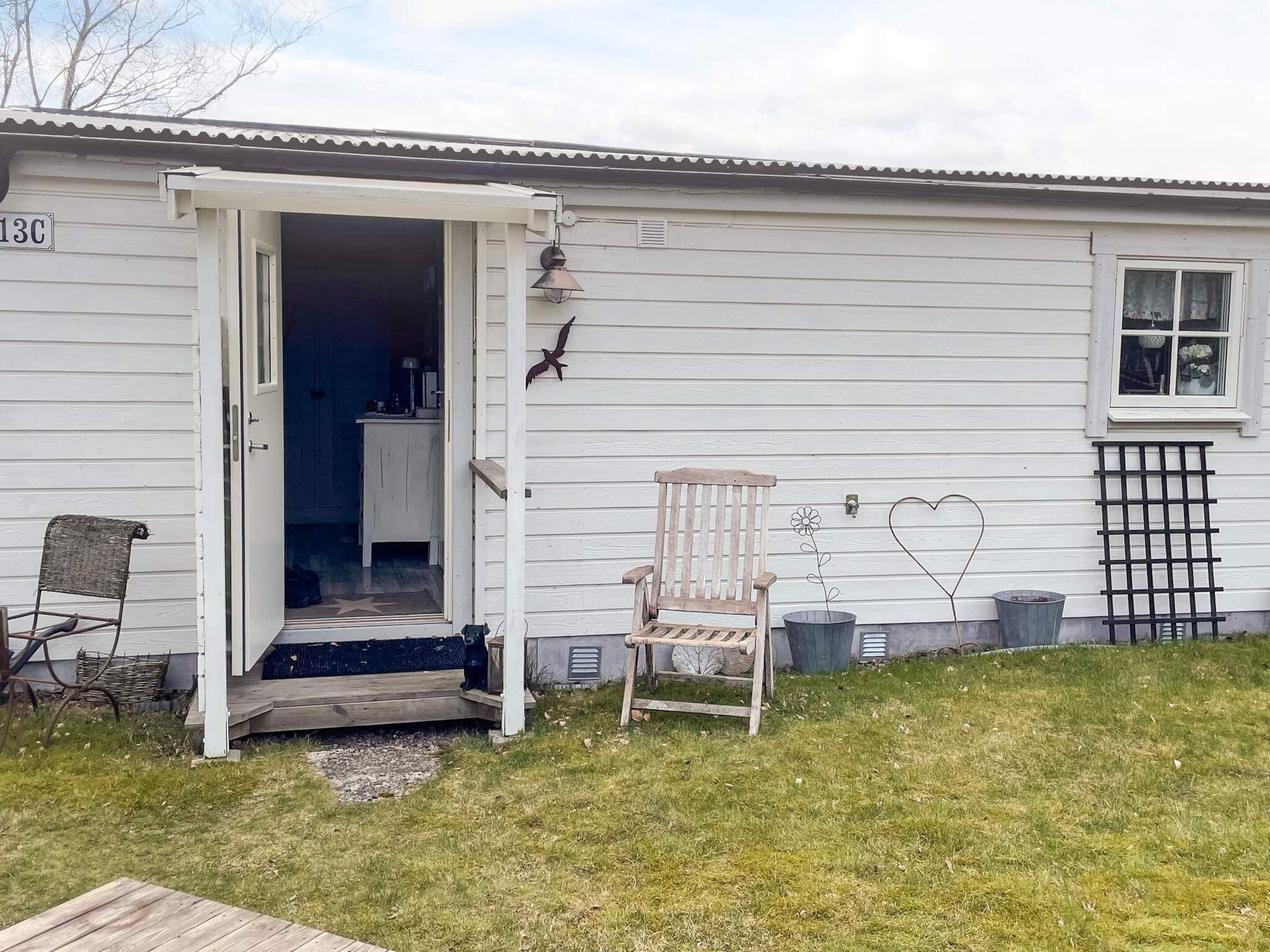 Et hus med en træterrasse, en stol, en hjerteformet pynt og en fugleskulptur.