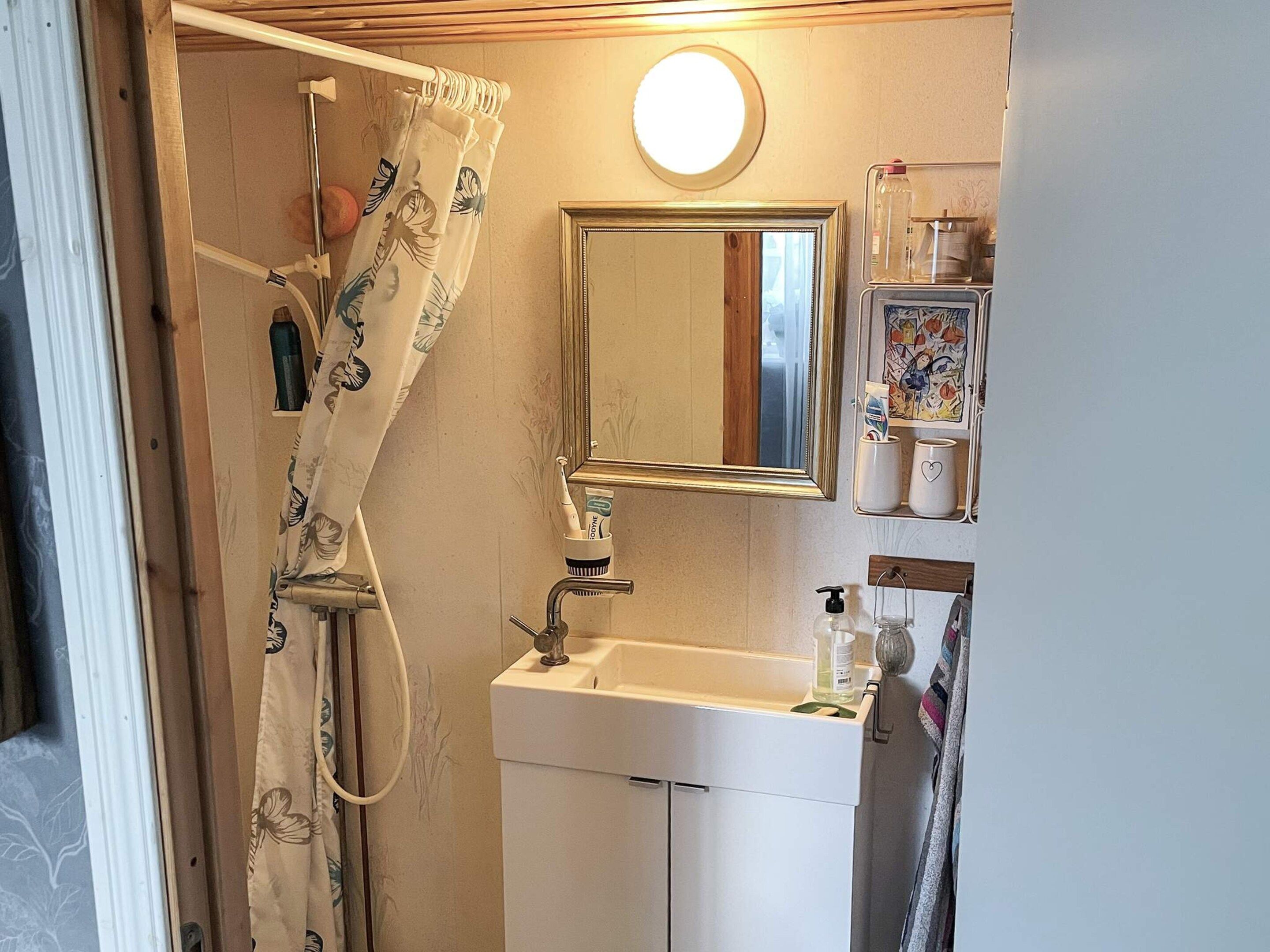A bathroom with a shower, a sink, a mirror, and a shelf with toiletries.