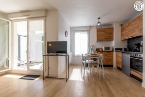 A modern kitchen with wooden cabinets, a built-in oven, and a dining area with a table and chairs. - Edelweiss A2 - ALBERTVILLE (ALBERTVILLE)