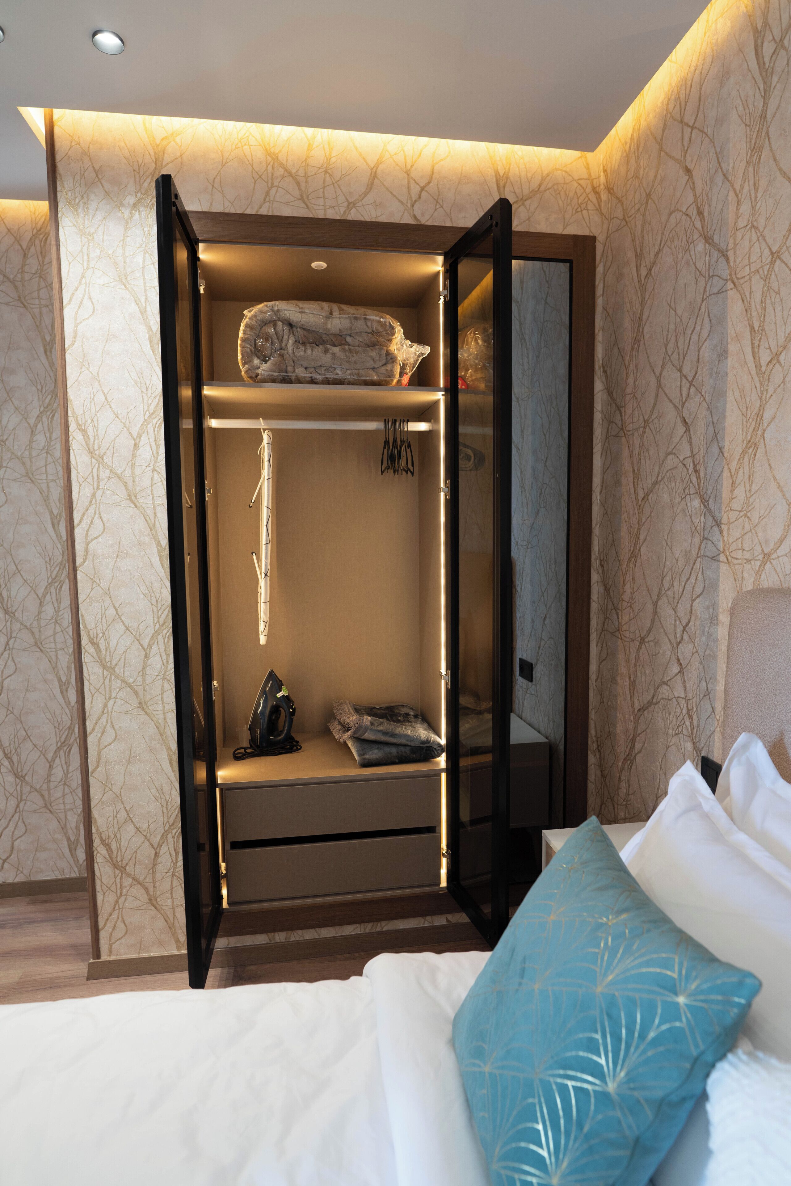 Une chambre à coucher avec un lit, un oreiller bleu, une armoire avec un miroir et un luminaire suspendu.
