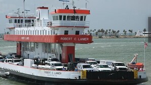 A ferry named 'Robert C. Lanier' with a white and red color scheme, docked at a port with vehicles and a clear view of the ocean and distant shoreline. - 1 or 2 Wonderful private RV spots,full hookups. 5 min walk to beach on Bolivar (Bolivar Peninsula)
