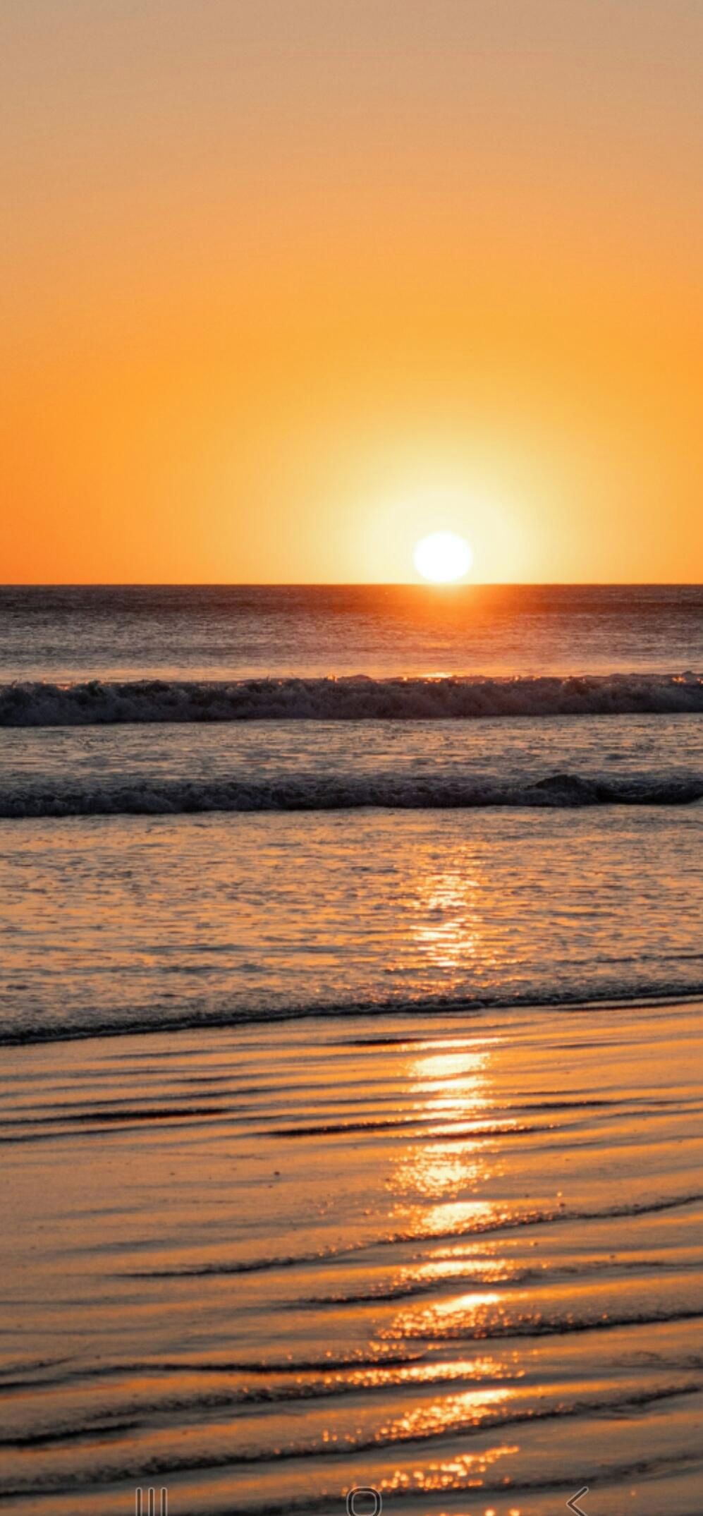 A sunset over the ocean with waves on the shore.