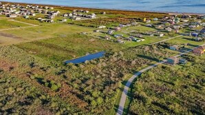 An aerial view of a residential area with houses, a small lake, and a road. - 1 or 2 Wonderful private RV spots,full hookups. 5 min walk to beach on Bolivar (Bolivar Peninsula)