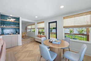 A modern interior with a dining area, a kitchen with blue-tiled backsplash, and large windows with views of greenery.