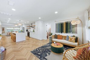 Amplia sala de estar con sofá, una mesa redonda y un comedor, con una cocina al fondo.