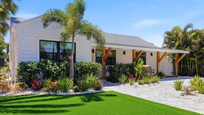 A modern house with a well-maintained lawn, a covered patio, and tropical plants. - 🦩Chasing Sunsets at St Pete Beach🦩 (Saint Petersburg)