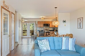 Una sala de estar con sofá, un comedor con sillas, una cocina con armarios de madera y vistas al exterior.