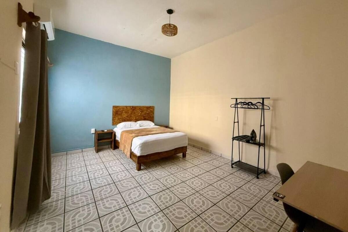 A hotel room with a bed, a small bedside table, a chair, a desk, and a wardrobe.