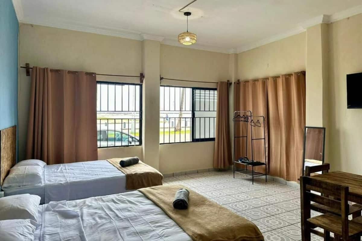 A hotel room with two beds, a desk, a chair, a coat rack, and a window with curtains.