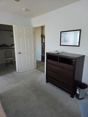 Ein Zimmer mit einem dunklen Holzschrank, einer weißen Tür, einem Stuhl und einem kleinen Mülleimer.