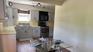 A modern kitchen with white cabinets, a stainless steel oven, and a glass dining table with a brown stool. - Perfect fit for FIFA World Cup visitors! 4-bedroom house in close-by Clifton (Clifton)