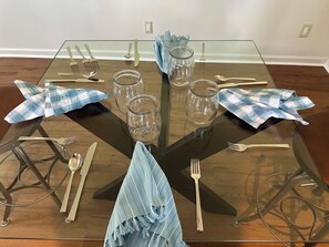 Ein Esstisch mit Glasplatte, umgeben von Metallstühlen, gedeckt mit Besteck und Gläsern.
