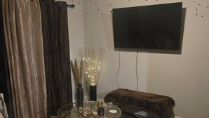 Un soggiorno con ventilatore a soffitto, televisore a schermo piatto, tavolino rotondo con oggetti decorativi, divano e una panca.