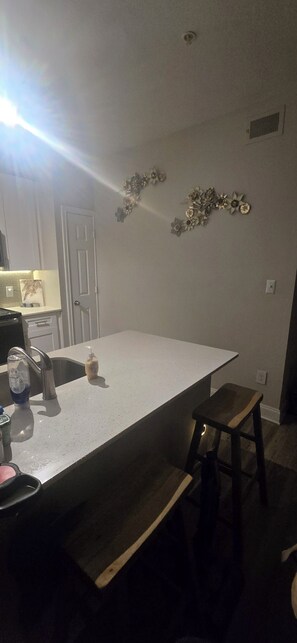 Una cocina con encimera blanca, un taburete de madera, un fregadero y decoración en la pared.
