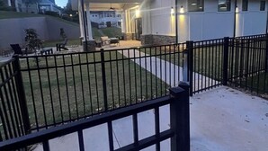 Un edificio moderno con un patio cubierto, un jardín cercado y vistas a otros edificios al fondo.