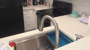 Una cucina con mobili bianchi, un frigorifero nero, un forno a microonde, una macchina da caffè, un frullatore e un lavello con una vasca blu.