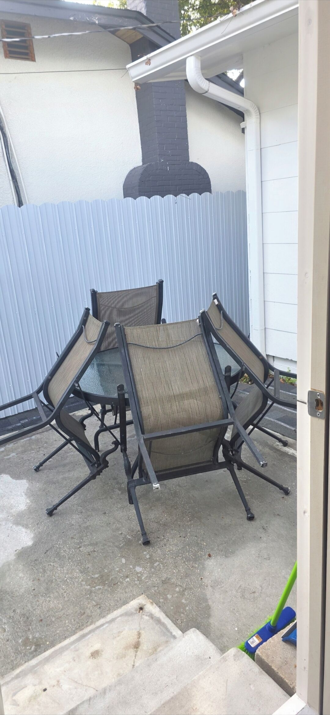 A patio with a table and chairs, a metal fence, and a building with a chimney.