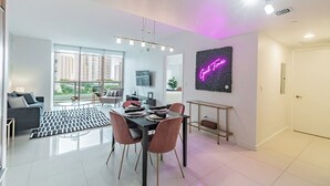 Ein modernes Wohnzimmer mit Essbereich, großen Fenstern, einer Neonreklame und einem minimalistischen Design.