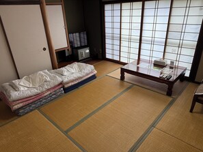 A traditional Japanese room with tatami flooring, a low wooden table, and a futon bed. - BungonoSato (Kusu)