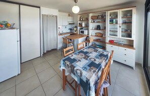 A compact kitchen with a dining table, chairs, a refrigerator, cabinets, and a microwave. - Appartment proche plage (Valras Plage)