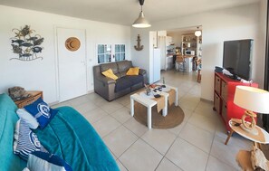 A living room with a sofa, a coffee table, a TV, and a kitchen in the background. - Appartment proche plage (Valras Plage)