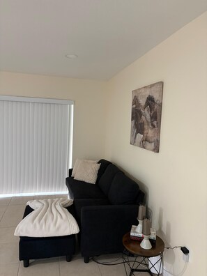 A living room with a black sofa, a white blanket, a small table with a lamp, and a painting on the wall. - Beautiful 3-bedroom house with AC in adorable New Port Richey (New Port Richey)