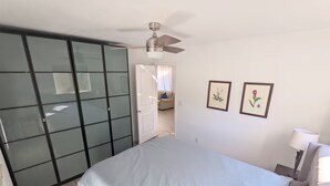 A bedroom with a bed, a ceiling fan, a wardrobe, and two framed pictures on the wall.