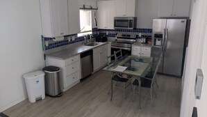 A modern kitchen with white cabinets, a stainless steel refrigerator, a microwave, and a glass dining table with chairs.