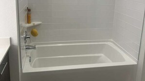 Ein modernes Badezimmer mit einer begehbaren Glasdusche, einer weißen Badewanne und einem kleinen Ablagebereich für Pflegeprodukte.