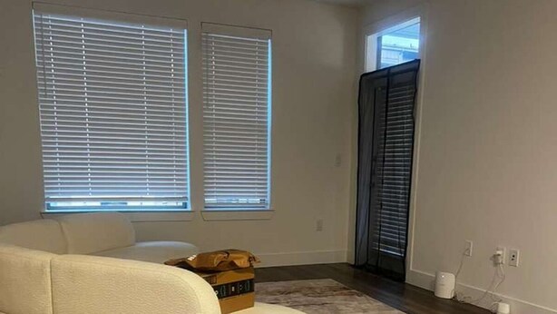 Ein modernes Wohnzimmer mit einer Eckcouch, einem Deckenventilator und einem großen Fenster mit Jalousien.