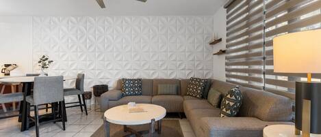 A modern living room with a sofa, coffee table, dining table, chairs, and a ceiling fan.