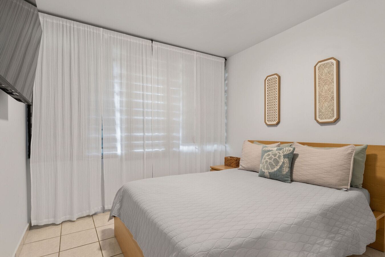 A bedroom with a bed, curtains, two wall-mounted decorative items, and a nightstand with a basket.