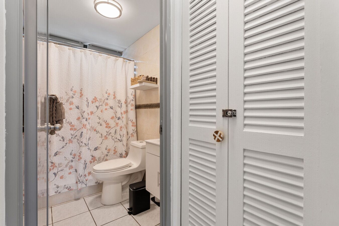 A bathroom with a toilet, shower curtain, and a trash bin.