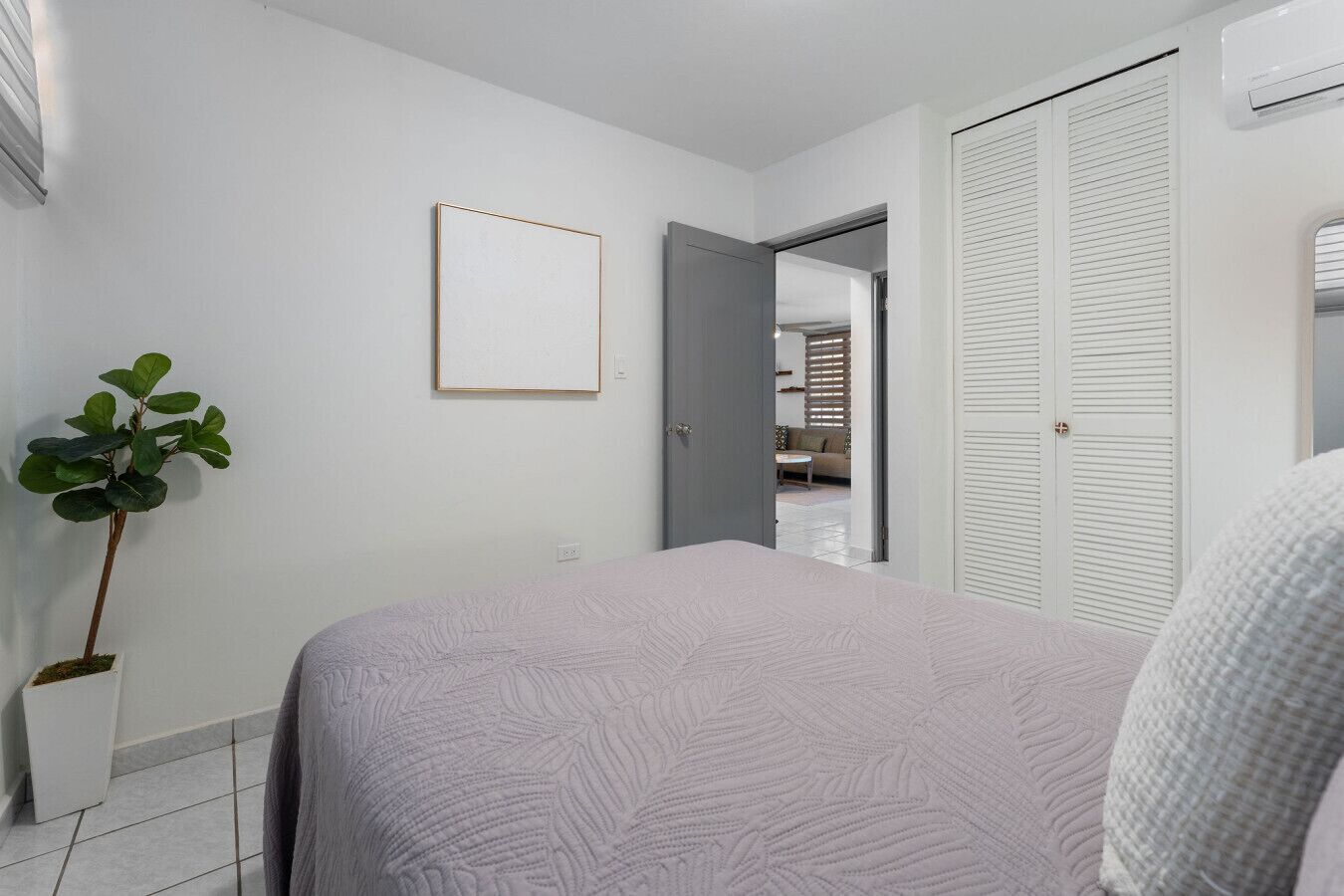 A bedroom with a bed, a potted plant, a wardrobe, and a door leading to another room.