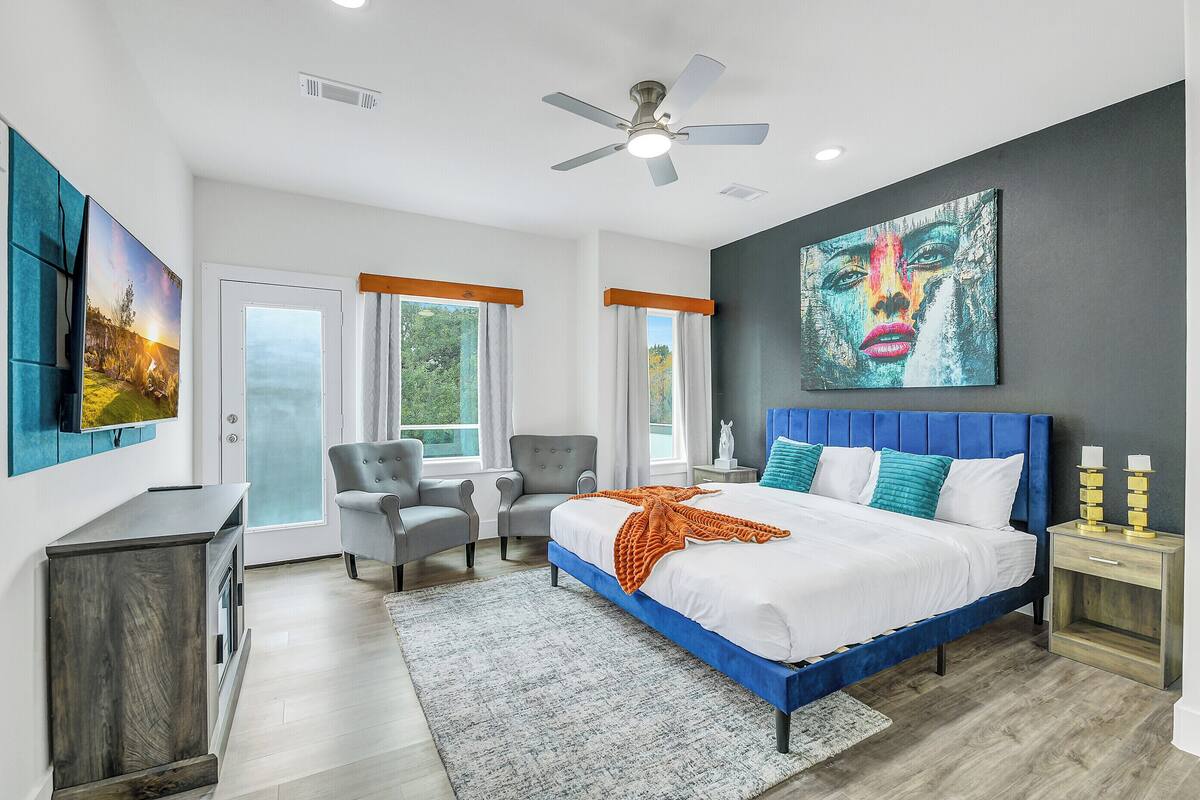 A modern bedroom with a large bed, a ceiling fan, and a painting on the wall.