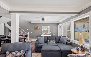 A modern living room with a sectional sofa, a dining area with chairs, a staircase, and a ceiling fan. - Lakeside Landing l 4-Season Adirondack Retreat (Northville)