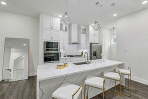 A modern kitchen with white cabinetry, a marble countertop, and bar stools.