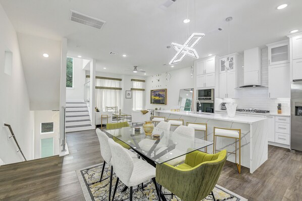 A modern kitchen with white cabinetry, a central island, and a dining area with a glass table and chairs.