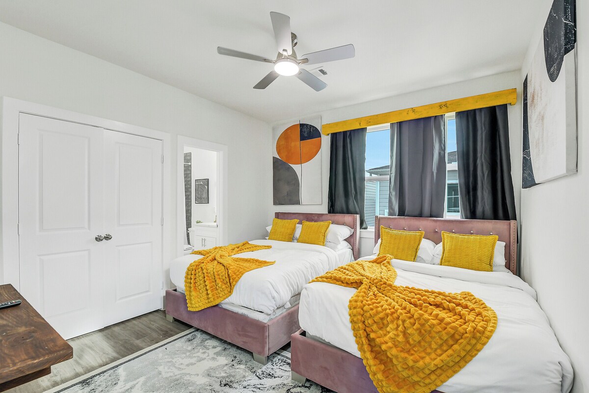 A hotel room with two beds, a ceiling fan, a large window with curtains, and a door.
