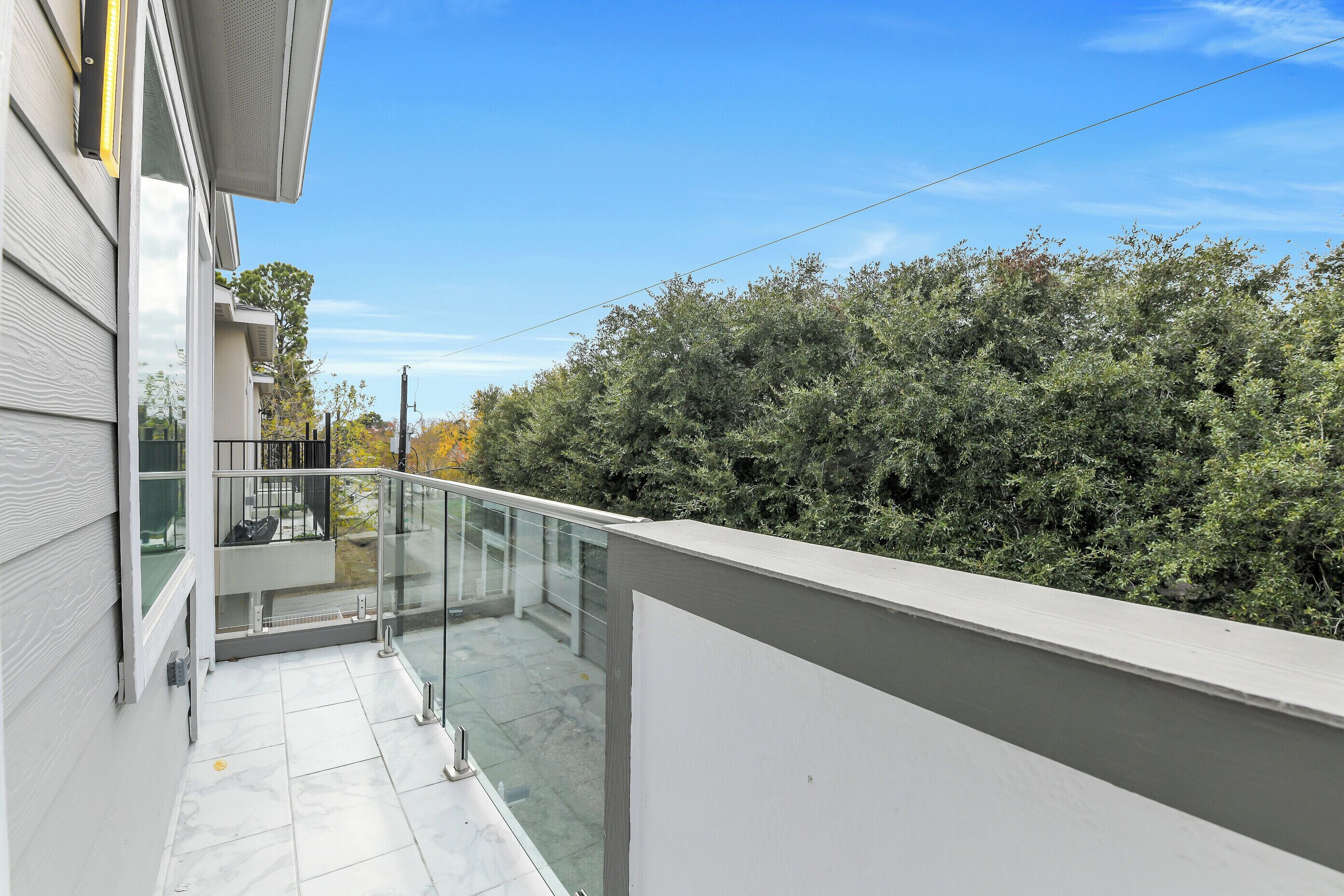 A balcony with a glass railing, a tiled floor, and a view of dense foliage.