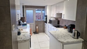 A modern kitchen with white cabinets, a marble countertop, a built-in oven, and a coffee maker. - Two bedroom independent house with parking & WiFi (Romford)