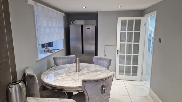 A modern kitchen with a marble countertop, stainless steel appliances, and a dining area with a round table and chairs. - Two bedroom independent house with parking & WiFi (Romford)